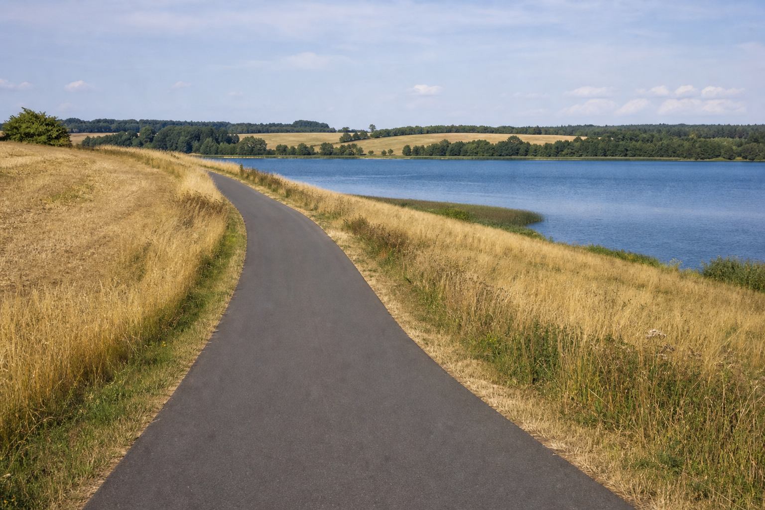 Radweg zwischen Feldern und blauem See in Nordostdeutschland